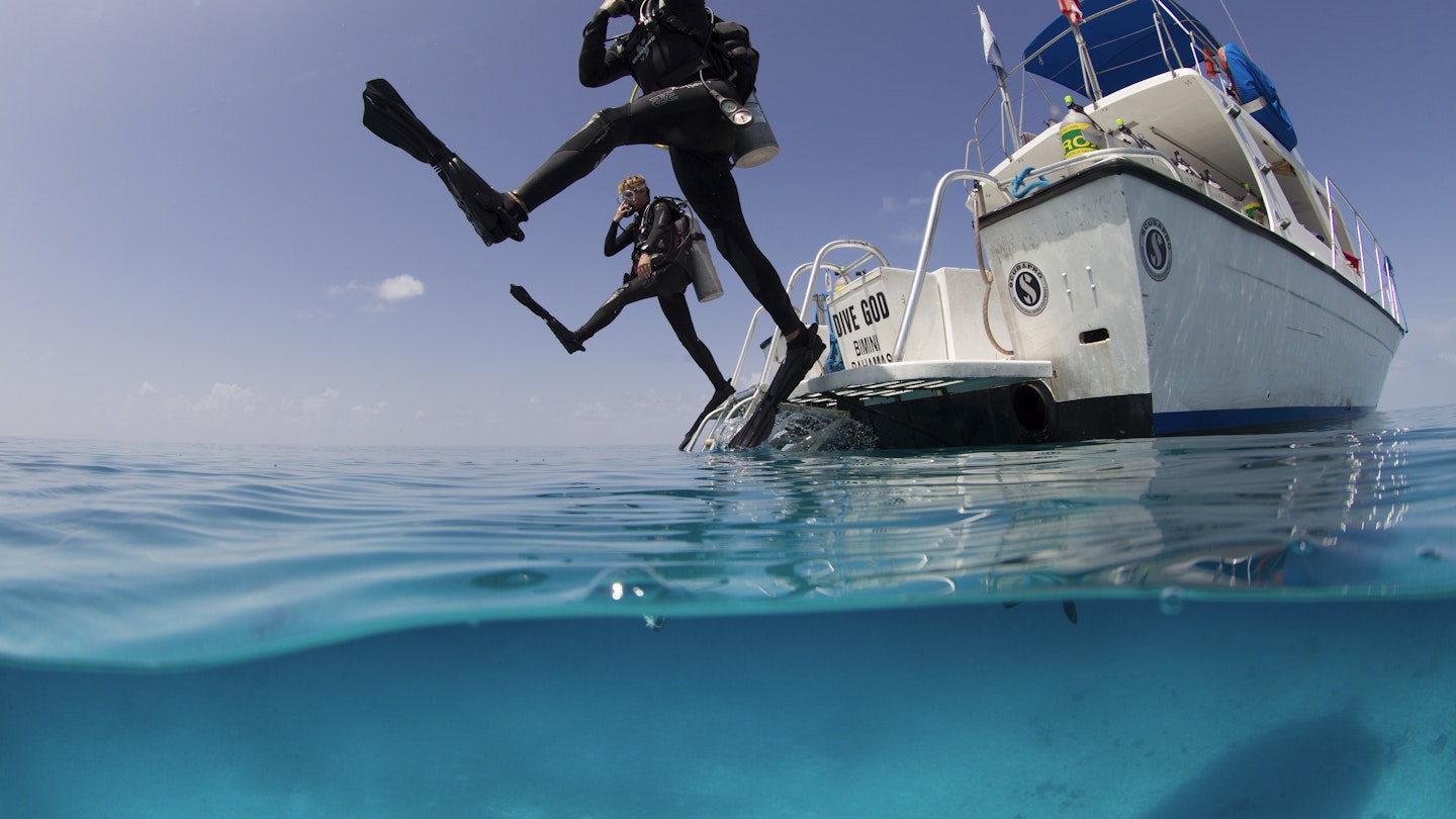 Over/under view showing divers performing giant stride entry into the clear calm waters of the Atlantic ocean.