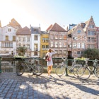 Woman traveling in Ghent old town, Belgium - stock photo
Sunrise view on the water channel with beautiful old buildings with woman standing near the bicycles in Ghent city