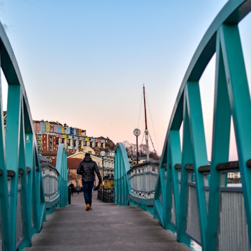 Man walking on Blue / Turquoise footbridge leading from Bristol Harbor towards the well known colorful houses of Clifton -Image; Shutterstock ID 1330383716; your: Sloane Tucker; gl: 65050; netsuite: Online Editorial; full: Destination Page
1330383716