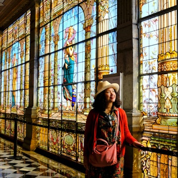 A tourist admiring the beautiful stained glass windows along a corridor inside Chapultepec Castle.