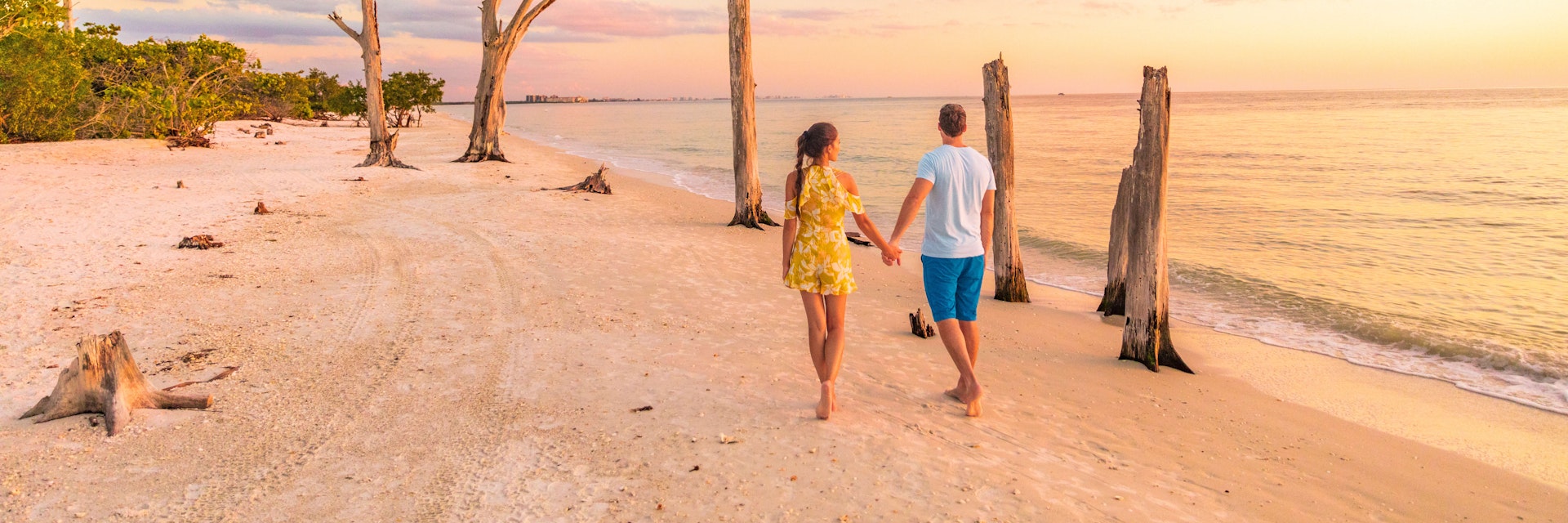 Couple walking on beach at sunset romantic travel getaway, idyllic Florida destination, Lovers Key State Park in the gulf of Mexico. Woman and man holding hands relaxing. Southwest Florida.