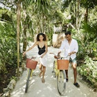 Wide shot of smiling couple walking bikes on pathway in jungle at tropical resort
1366306661
exotic travel
A woman and man walking along a path with bikes in Mexico