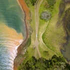 Dominical, Costa Rica - An aerial view of a car driving along a dirt road surrounded by water on either side.  © Jordan Siemens / Getty Images