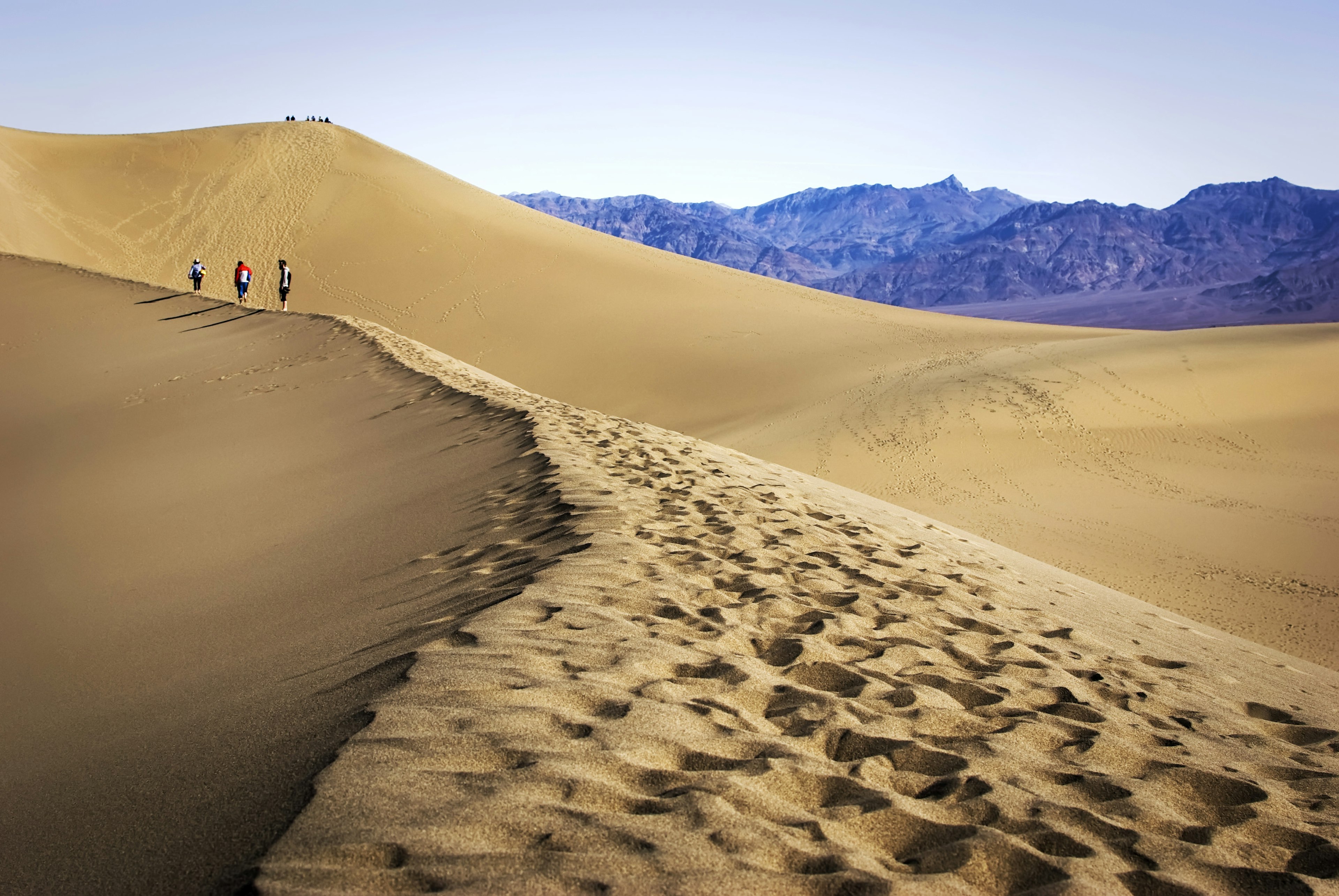 People walking on vast sand dunes with mountains in the distance