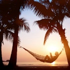 Silhouette of a woman relaxing in a hammock on a beach during sunset. 