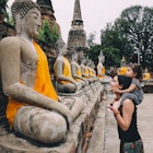 Ayutthaya, Buddha statues in a row in Wat Yai Chai Mongkhon, mother and daughter in front of a Buddha statue.