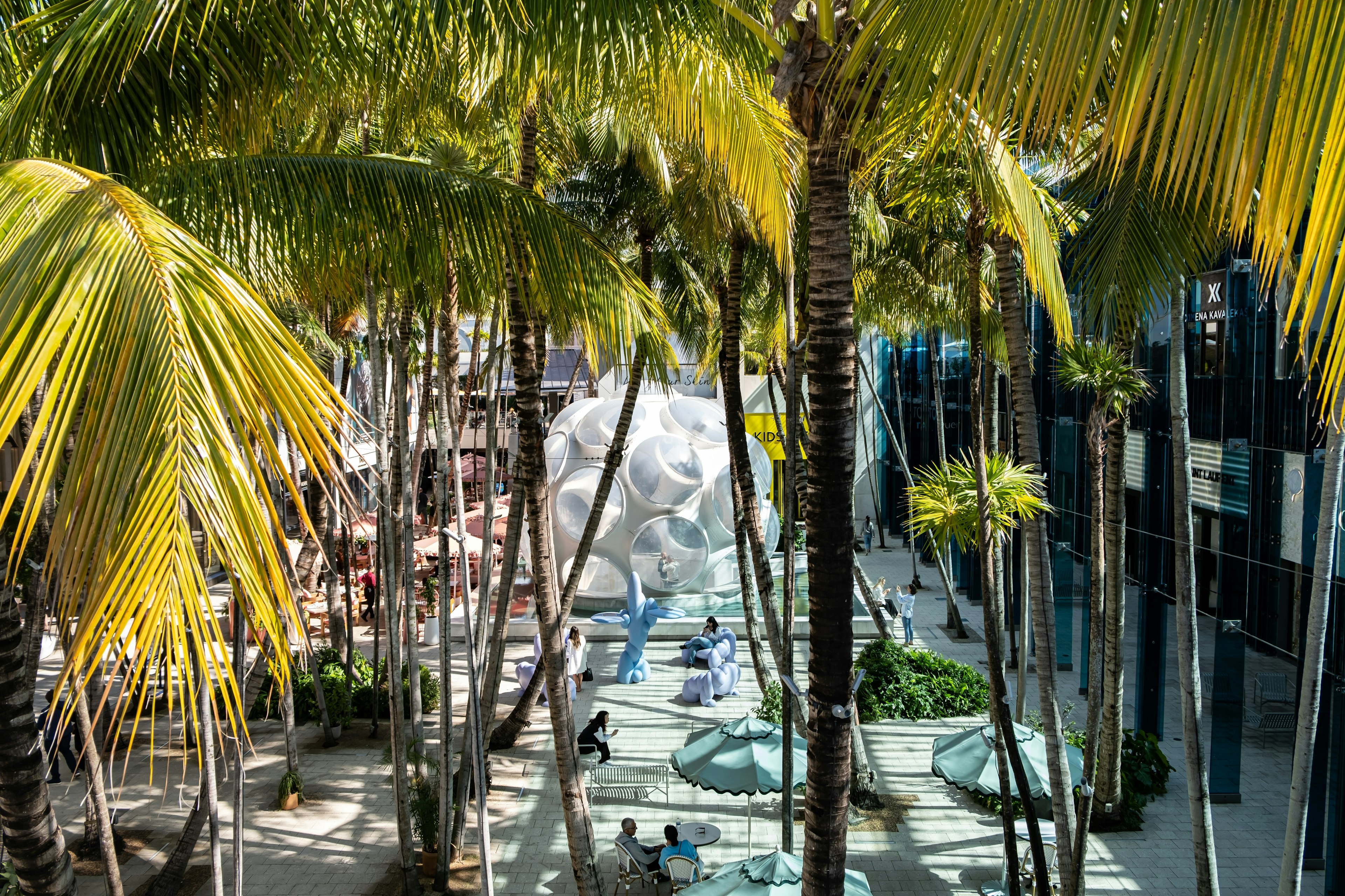 A large plastic sphere with bulging windows sits in a square lined with palm trees