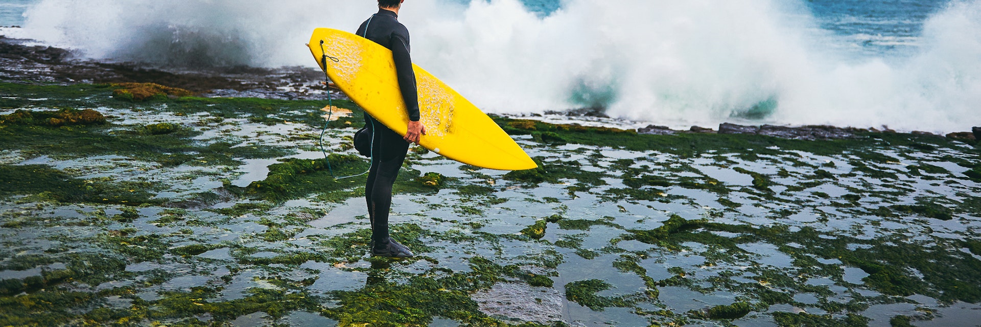 Surfer looking at the waves crushing on the cliff during winter surfing session