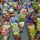 Crowded wooden boats in canal with fruits, vegetables, foods and grocery products for sell and trade by villagers at Tha Kha traditional floating market.