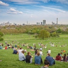 London, UK - April, 2018. Breath-taking panoramic scenic view of London cityscape seen from a crowded Primrose Hill park on a sunny spring afternoon.