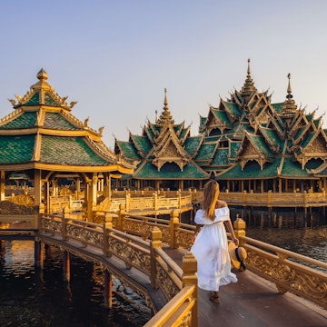 Woman walking on a bridge to Buddhist temple in Thailand during sunset.